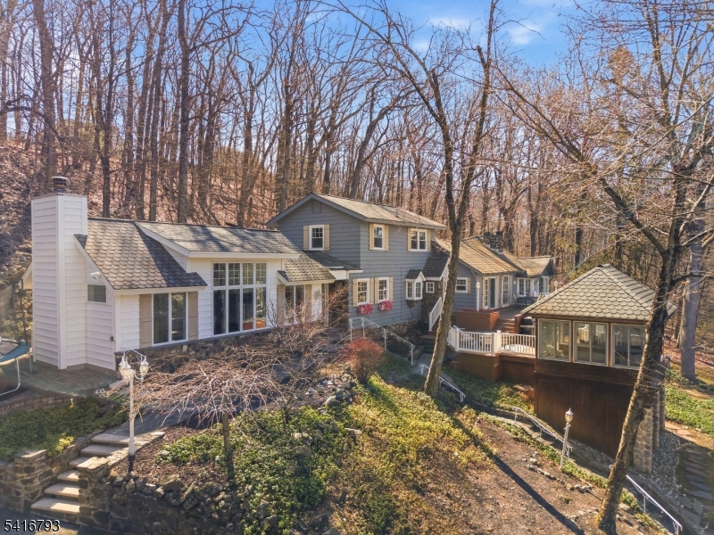 Lake Mohawk custom lake-style home set on .87 private acres with seasonal lake views and an abundance of outdoor living spaces. This inviting property offers multiple areas to relax and entertain, including expansive decks, a patio, a three-season gazebo, and a fire pit area, all designed to enjoy the peaceful natural surroundings. Inside, the exquisite kitchen features ceiling-height cabinetry, granite countertops, a center island, and stainless-steel appliances, blending style and functionality. Large windows fill the home with natural light and create a seamless connection to the outdoors. Both the living room and family room feature cathedral, beamed ceilings and wood-burning fireplaces, creating warm and dramatic gathering spaces. The first-floor primary suite offers comfort and convenience with a private sitting room and ensuite bath. Upstairs you will find two additional bedrooms and a full bath. The home also includes a whole-house generator for year-round peace of mind, along with a detached 2-car garage, plenty of parking, and a designated area to keep your trailered boat. This charming house features a fairy-tale inspired design, giving it a magical and storybook-like appearance. The most striking element is its unique roof, which slopes gently toward the center, creating a whimsical and eye-catching shape.   Located close to Beach 6.  Only 2 miles to the center of Lake Mohawk.  New septic to be installed. Deck and fireplaces, "as is" condition.