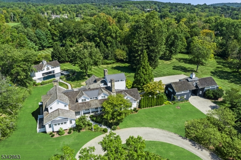 Tucked away in the picturesque landscape of Far Hills, within an hour of NYC, this extraordinary country estate provides an exquisite blend of rustic charm and modern luxury. Set on 10+ gated acres, this private retreat offers natural beauty, architectural excellence, and refined craftsmanship. An extensive 2005 rebuild resulted in a stunning 6-bedroom residence. The spacious home, with two 1st-floor suites for guests, is defined by hand-crafted millwork and hardwoods that adorn the interior. The newly updated chef's kitchen features radiant-heated floors, state-of-the-art appliances, custom cabinetry, and a breakfast bar. The adjacent great room, crowned by soaring hand-hewn beams, serves as the heart of the home, with a floor-to-ceiling stone fireplace and walls of windows that invite in natural light. The primary suite is a serene retreat, complete with a tower office with breathtaking views of the estate's gardens and rolling lawns. The deer-fenced property includes a pool, pool house, tennis court, reflecting pond with fountain and entertainment patios with a hot tub & outdoor kitchen. The carriage house presents a 4-car garage, office, gym, and full bath. This extraordinary home showcases an exterior of fieldstone, hand-split cedar roofing, copper gutters, fieldstone chimneys, and covered porches. Far Hills offers a coveted lifestyle with its equestrian heritage, scenic countryside, world-class golf courses, top-rated schools, fine dining, and access to NJ Transit.