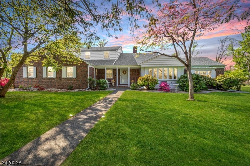 Nestled in the sought-after Van Wyck Brooks section of Plainfield, once known as Presidential Way, this expansive raised and extended ranch sits on approximately 1.7 acres of beautifully landscaped grounds. This home showcases exceptional craftsmanship with steel I-beams, oversized wood beams, solid brick construction, and enduring materials rarely found today. Offering 5 bedrooms, 3 full and 2 half baths, the layout is ideal for multiple private living zones, featuring a first-floor bedroom suite, a flexible west wing (formerly a dental office), and a finished basement with multiple private living zones. The gracious entry leads to a large, light-filled living room with expansive windows, gleaming floors, and a gas fireplace. The formal dining room features parquet floors, built-ins, designer wallpaper, and a striking solid brass chandelier. 3/4-inch Brazilian cherry floors extend through the main living areas, hallways, office, and select bedrooms. The lower-level family room adds flexible living space. The updated eat-in kitchen offers granite countertops, stainless steel appliances, quality cabinetry, and a breakfast area. A screened porch overlooks private, park-like grounds with mature plantings. Additional features include a new roof and gutters (2020), two-zone hot water heating, copper plumbing, central air (west wing), wall units (east wing), an oversized 2-car garage and a driveway that can hold 4-5 cars. Close proximity to the bus and train station going to NYC.
