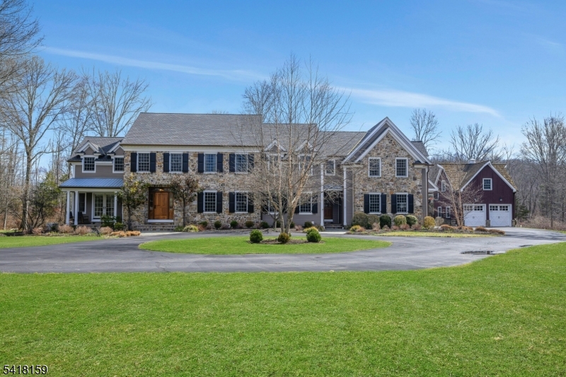 Blending timeless architectural elegance with modern luxury, this classic Bucks County-style residence is nestled on nearly three landscaped acres on Mendham Township's sought-after east side in the heart of Washington Valley. Bordering tranquil parkland, it offers a rare combination of privacy, serenity, and refined living. Defined by a natural fieldstone and cedar exterior, this 5 bedroom, 4.3 bath home showcases exceptional craftsmanship, custom millwork, and inviting interiors designed for everyday comfort and effortless entertaining. At the heart of the home, a spacious chef's kitchen with premium appliances and a large center island flows into the family room featuring a stone accent wall and gas fireplace. The formal dining room with butler's pantry and the wood-paneled library with custom cabinetry add elegant dimension. A sunlit billiards room with with wet bar extends the home's entertaining space. Upstairs, five ensuite bedrooms include a luxurious primary suite with sitting room, tray ceiling, built-ins, and gas fireplace framed by stone surround and hearth. The finished lower level offers a wine room, media room with theater seating, fitness space, and recreation area. A three-car attached garage is complemented by a two-bay carriage house with an unfinished upper level. Outdoors, a heated pool with raised spa and waterfall, built-in gas grill, and gas fire pit create a private resort setting, just minutes to Morristown and the NYC direct train line.