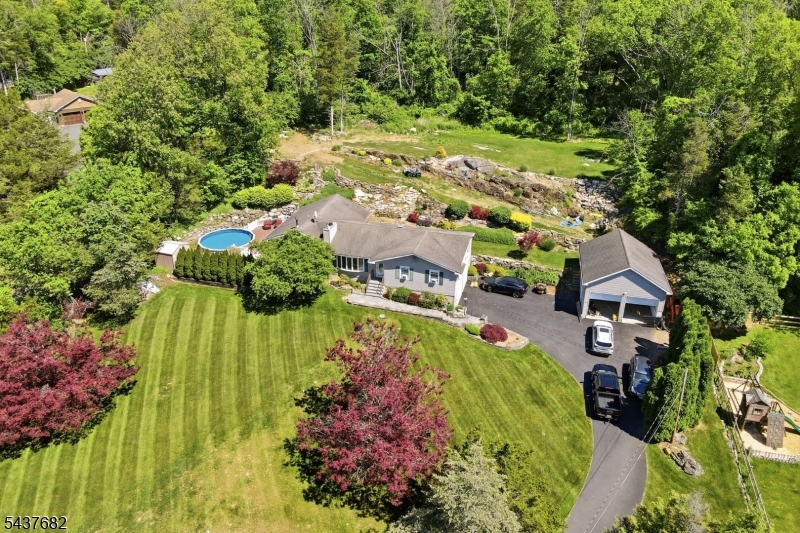 Set back on 1.5 +acres, this beautiful oversized ranch is situated on a park like property. Featuring a built-in pool, full walkout basement, attached two-car garage, and an incredible oversized detached garage with loft and is complete with a lift and compressor (both inc). This property presents a rare opportunity for car enthusiasts, hobbyists, contractors seeking  workspace and storage. The exterior has vinyl siding, shutters, natural stone retaining walls, walkways, and front steps. Inside, the spacious living room is anchored by a wood-burning fireplace and large bay window. The expansive eat-in kitchen offers granite tops, a center island, abundant cabinetry, and a bright dining area with a bay window overlooking the backyard, plus hardwood floors throughout. The family room has soaring ceilings, a wood-burning stove, and sliding doors leading to the deck and built-in pool, creating the perfect space for both everyday living and entertaining. Plus, just off the family room is a den that can serve as a home office, guest room, or potential fourth bedroom. A nearby full tiled bath offers flexibility for a guest suite. The bedroom wing includes three comfortable bedrooms and a tiled full bath with tub / shower. First floor laundry / mudroom has pantry storage and direct access to the backyard.Recent improvements include a new septic field and lid (2025), new garage doors (2025), newer driveway (2023), and well pump (2019).