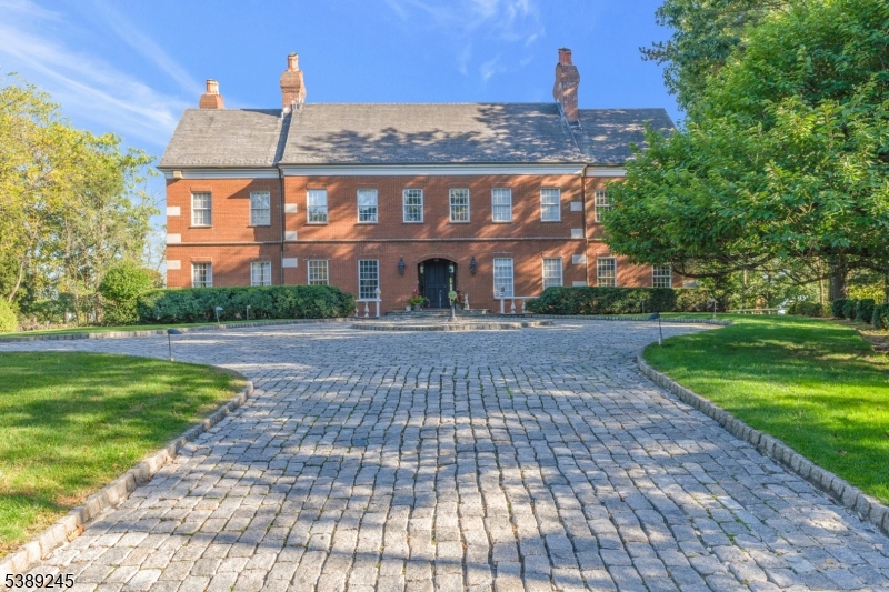 This 'one of a kind' residence is unlike anything in the coveted Boro of Watchung. Situated at the end of a glorious cul-de-sac of custom homes lies our subject. This 4-sides brick masterpiece towers over Johnston Drive offering winter views from its lofty perch. The cobblestone driveway leads to an 11 vehicle garage with 4 door bays; then descends to a stone, grotto-like, passageway to the rear grounds, spa and regulation tennis court. It's essentially impossible to adequately describe the grounds; though the images will offer a sense of this old world, European-type grandeur. Once inside the warm and engaging confines of the Butternut paneled foyer; an interior of large, distinctive rooms unfolds. Ten foot ceilings run throughout the 1st level where French doors lead to adjacent spaces while lots of glass offer views and egress to the rear lawn, patio area and the aforementioned spa and tennis court. Eight rooms are sprawled out over the home's massive 1st level along with 3 fireplaces & a pizza oven. Five bedrooms, 5 baths & 3 more fireplaces are found on level ll. The enormous primary suite features 2 separate baths, a dressing room, a fireplace, walk-in closets, a volume ceiling and a dressing/sitting lounge. Four additional bedrooms are nicely served by 3 full baths inclusive of an ensuite with a wrap-around loft. The ground-level basement houses 11 vehicles, though it may just as easily serve as a massive recreation area while still accommodating 4 full sized vehicles.