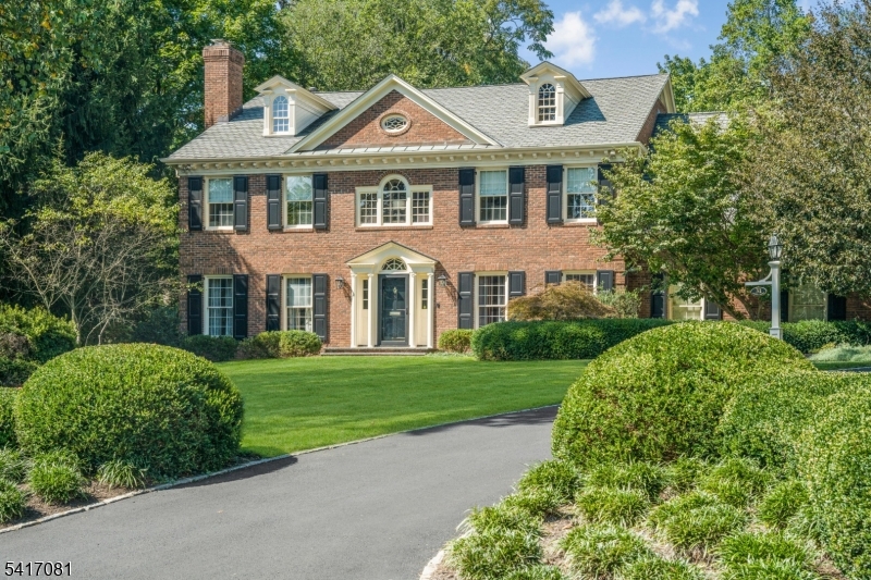 Set back from the street with a long tree-lined approach, this timeless Georgian brick Colonial makes an immediate impression with its symmetry, scale and quiet confidence. Ideally located in one of the most coveted in-town settings, the home offers rare proximity to the train and local schools -- an exceptional convenience that elevates everyday living. Mature trees, manicured hedges and lush lawns create a sense of arrival that feels both private and refined, while extensive millwork, custom built-ins and elevated finishes reflect consistent quality throughout. Built in 1989, this residence stands apart in a neighborhood known for much older homes, offering the comfort, layout and infrastructure of more modern construction while honoring classic architectural details. A columned portico opens to a gracious center hall, flanked by formal living and dining rooms. The rear of the home unfolds into an expansive family room, breakfast room and kitchen inspired by Clive Christian design. A first-floor library with full bath offers flexibility as a bedroom suite while upstairs each bedroom is thoughtfully positioned and paired with its own bath, including a spacious primary retreat with luxurious bath and custom walk-in closet. The finished lower level offers areas for media, office, exercise, wine storage and more. Outdoors, a bluestone patio overlooks a deep level lawn framed by mature landscaping -- private, serene and perfectly suited for entertaining or quiet moments at home.
