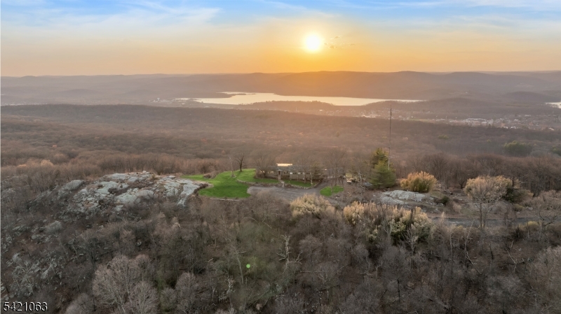 A one-of-a-kind mid-century modern with an unmistakable Hollywood Hills sensibility, set high along the ridgeline of the Ramapo Mountains at the end of a nearly mile-long cul-de-sac, surrounded by an expansive protected mountain landscape, with panoramic views spanning the Wanaque Reservoir, the surrounding range, and the New York City skyline.The only residence at the end point, the home is defined by its position, elevation, and perspective. Built in 1960, it was designed around the view, with walls of glass, a double-sided fireplace, and original knotty pine tongue-and-groove paneling and ceilings defining the main living spaces. Period-specific elements remain intact throughout, reflecting the home's original mid-century design and reinforcing its architectural consistency. A glass-enclosed indoor pool sits directly along the primary view line, fully exposed to the landscape beyond. It is a defining architectural element of the home and central to its original design. Five bedrooms and two full baths, along with a greenhouse, large workshop, attached four-car garage, and an additional open garage structure below, complete the property. Set above the surrounding landscape, the setting offers a high degree of privacy and separation, with New York City within easy reach.