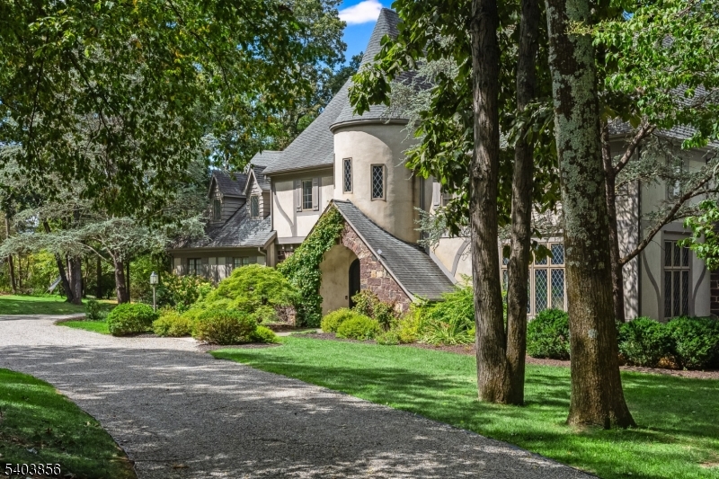 Tucked away in picturesque Far Hills, within an hour of Manhattan, this updated French Normandy Tudor-style residence, set on 14 acres, is a rare architectural gem, blending storybook charm with timeless sophistication. From the long private drive, the signature turret entry immediately sets the tone, with diamond leaded-glass windows and classic European detailing. The facade showcases hand-laid fieldstone, half-timbering, smooth stucco, and steeply pitched rooflines. Inside, the light-filled home offers 9 -ft ceilings, spacious rooms, hardwood floors, updated baths, and finely crafted details. The dramatic entry hall has a soaring 36-foot turret, exposed beams, patterned flooring and curved staircase. Living spaces include a stunning, generously scaled living room, a large dining room, a wood-paneled library with fireplace, and a chef's kitchen. The adjacent family room with a fireplace opens to an expansive rear deck overlooking the pond. Upstairs, four of five bedrooms include a luxurious primary suite with two walk-in closets and dual updated baths. A finished walk-out lower level adds a family room, office, bedroom, game room, wine storage, full bath, and laundry. The grounds feature mature trees, lush landscaping, a one-acre pond with a fountain, a gunite pool and spa, a tennis pad, a heated 10-vehicle car barn, and deer fencing. Close to the village, NJ Transit, major highways, world-class golf, dining, equestrian facilities and just 30 mins to Newark Liberty Airport