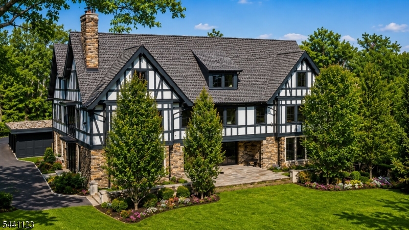A masterwork where gallery minimalism meets Montclair grandeur, this modern Tudor estate reimagines a storied 1910 Van Vleck & Goldsmith landmark for the way we live now. Taken down to its original stone and timber shell in 2020, architects Robert Gurney & Jonathan Perlstein inspired the residence's meticulous reinvention by award-winning Brinton Brosius Contractors alongside interior designer Birgitte Pearce, creating a light-filled retreat that quietly dissolves the line between inside and out. Soaring ceilings, expansive walls of glass and a three-story atrium anchored by a sculptural floating staircase set a tone of contemporary European refinement, layered with bespoke lighting and richly textured surfaces. The main floor centers on a dramatic living and dining hall framed by a monumental fireplace and original stone walls, while a generous kitchen and family room flow through a wall of sliding glass to a gracious patio, intimate stone porch and secluded garden with salt-water pool. Upstairs, serene bedroom suites include a luxurious primary retreat reminiscent of the finest luxury hotel. The uppermost level offers a grand great room, fourth bedroom suite and future fifth bedroom suite. Below, an indoor salt-water pool, gym, sauna, steam room, recreation space and full bath create a private wellness sanctuary. Set on 1.8 lush acres offering expansive lawns, a three-car garage and a beautifully restored two-bedroom, two-and-a-half-bath carriage house with elevator.