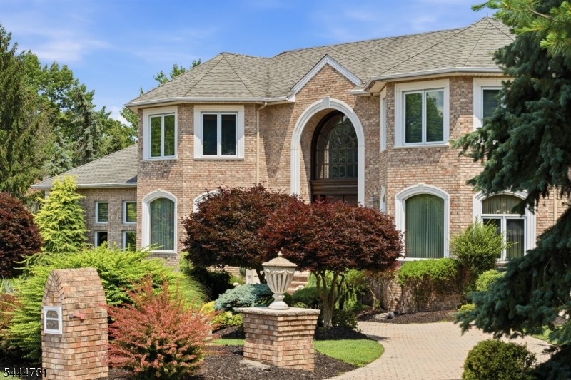 A grand brick residence with resort-style grounds, this home makes an unforgettable first impression with manicured landscaping, a circular paver approach and a dramatic arched entry. Inside, a two-story foyer sets the tone with stone floors, a sweeping staircase, wrought-iron details, custom millwork and a striking light fixture. Elegant formal spaces unfold from the entry, including a soaring living room with columned detail, an expansive dining room and a richly finished office with built-ins. The kitchen is designed for scale, with custom cabinetry, stone counters, premium appliances, a large island, extensive storage and a generous breakfast area wrapped in windows. Nearby, the family room offers warm wood floors, a fireplace, impressive ceiling height and direct access to the outdoor living spaces. The main level also includes a private bedroom suite, ideal for guests or extended stays. Upstairs, a gracious landing overlooks the foyer and leads to multiple bedroom suites, including a substantial primary retreat with a sitting area, large walk-in closet and spa-like bath with soaking tub, dual vanities and oversized shower. The lower level expands the home with a recreation room, billiards area, bar, secondary kitchen, bedroom, full bath and abundant storage. Outdoors, mature trees and layered plantings create a private setting with manicured lawns, a large terrace, outdoor kitchen, pool, spa and rock waterfall. A rare blend of presence, scale and everyday resort living.