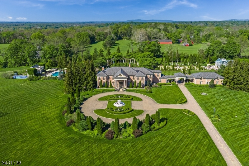 Approached through dual gated entrances and a winding, tree-lined driveway, this breathtaking 10,500-square-foot brick manor, by architect Doug Coleman, stands as a timeless statement of sophistication and privacy. Nestled on 25 rolling acres in prestigious Far Hills the estate offers a rare combination of architectural grandeur, refined interiors, and idyllic natural beauty. The residence features 6 elegant bedrooms, 9 full baths, 3 powder rooms, each space crafted with exquisite attention to detail. Soaring ceilings, oversized moldings, and luxurious finishes define the interior, while 7 fireplaces provide warmth and ambiance throughout. The home's stately presence is complemented by a slate roof and expanses of glass that frame panoramic views of manicured lawns and formal gardens. Every room exudes a sense of scale and proportion, from the grand formal spaces to the more intimate, private retreats. The lower level serves as a destination of its own, complete with a full kitchen, full bath with sauna, powder room, gym, office, family room, wine cellar, wine preparation area, and a tasting room ideal for elegant entertaining or relaxed leisure. Beyond the main residence, the property unfolds into an enchanting landscape of rolling hills, gentle streams, & formal gardens visible from nearly every rear-facing room. Outdoor amenities include resort-style pool, pool house, and an oversized conservatory surrounded by bluestone patios enjoying sweeping vistas. Elevator