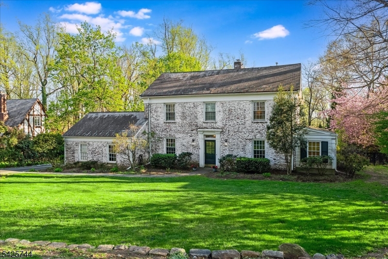 Nestled in the prestigious Spring Brook neighborhood, this timeless 1930s Colonial blends historic charm with modern luxury. Set on a sought-after street, the stately brick home showcases exceptional craftsmanship, a classic slate roof, and professionally designed hardscaping for enduring curb appeal.Designed for elegant living and effortless entertaining, the home offers refined yet inviting spaces. The gourmet kitchen features a Viking six-burner range with pot filler, custom cabinetry, and a granite island with seating. It flows seamlessly into a formal dining room with gleaming hardwood floors and a gracious living room with a fireplace. A private office provides a quiet retreat, while the sun-filled, sunken family room with its own fireplace opens through French doors to an expansive bluestone patio, ideal for indoor-outdoor living.The primary suite is a true sanctuary with 11-foot ceilings, a spa-inspired bath, walk-in closet, and Juliette balcony. Three additional bedrooms and updated baths offer comfort and style, complemented by detailed moldings and hardwood floors throughout.The finished walkout lower level adds versatility with a recreation area, second family room, and powder room. Set on .44 manicured acres with tiered lawn and mature evergreens, this move-in ready home offers privacy and timeless appeal.