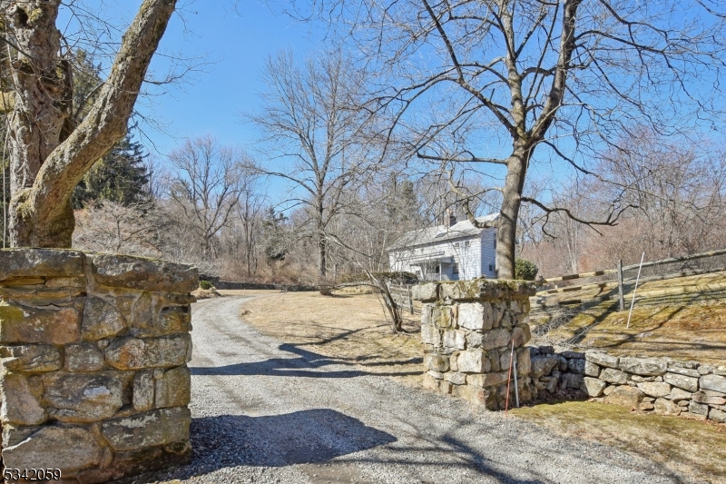 This beautifully renovated and expanded carriage house, nestled on over 5 acres of lush, private land, strikes the perfect balance between tranquility and convenience. Just 1 mile from vibrant downtown Bernardsville and the train station, this home offers easy access to all the amenities you need while maintaining the peace and privacy of a country retreat. The spacious, thoughtfully designed layout blends historic charm with modern upgrades. The first floor features a guest bedroom with an en suite bath, providing a comfortable and private space for visitors. Additionally, a well-appointed home office offers a quiet, productive environment. The large terrace seamlessly connects the indoor living spaces to the outdoors. Step outside to enjoy the custom PebbleTec pool, surrounded by beautifully landscaped grounds, with a tranquil pond enhancing the peaceful ambiance of the property. Inside, the open-concept living area is ideal for hosting guests and entertaining. The second floor includes four spacious bedrooms, including a large primary suite with an en suite bath. A bonus loft area on the third level offers endless possibilities perfect for a home office, play area, or additional living space. The property also features a detached 2-car garage, complete with a climate-controlled gym and game room, offering even more space for relaxation and recreation. With its perfect combination of luxury, location, and functionality, this property is truly one-of-a-kind.