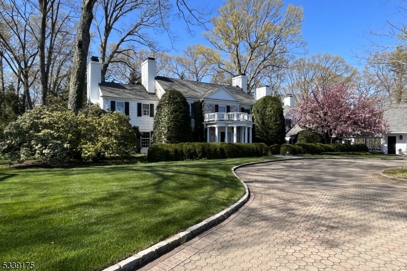 This meticulously maintained residence offers exquisite interiors, beginning with a grand columned portico and balcony. Formal rooms and casual spaces are enhanced by tall windows, crown moldings, wainscoting, window seats, and oak floors. The sunken living room, with its pegged oak floor and marble-framed wood-burning fireplace, reflects the home's colonial inspiration. French doors open from the adjoining Dining Room, with hidden pantry, to a front-to-back Garden Room, with tall windows and a slate floor offering serene views of the gardens and patios.The updated 2023 Kitchen features Danby white marble countertops, custom cabinetry, dual prep stations, and a walk-in pantry, with top-tier appliances like DCS, Sub-Zero, and Bosch. The breakfast area overlooks the grounds.The Family Room, with cherry wood beams, built-ins boasts a wood-burning fireplace. Two sets of double doors open to the grounds. Upstairs, the Primary Suite includes a marble bath and renovated Dressing Room. A second en suite with new marble bathroom and three more bedrooms and hall bath offer comfort and privacy. The finished lower level includes a leisure room, gym, office, wine cellar, and utility rooms.Practical amenities include multiple closets, a Laundry Room, and a glass-enclosed breezeway to the massive Garage, which offers four bays, five doors, built-in cabinetry, and loft access. The property is ideally located in Harding, Morris County, with easy access to major highways and Manhattan.