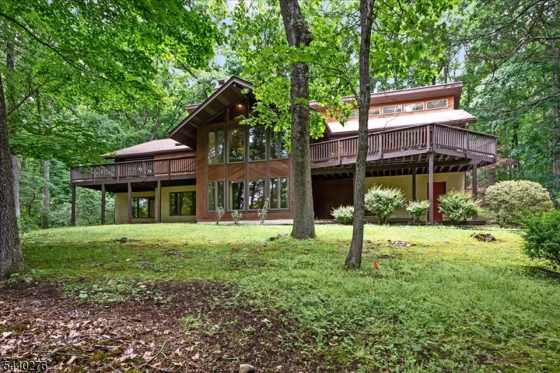 Tucked into a private wooded setting with seasonal mountain views, this distinctive retreat offers nearly 4,000 SF of living space and a unique blend of rustic charm and contemporary design. Custom windows frame the surrounding landscape with seasonal views and fill the home with natural light, while soaring vaulted ceilings create an airy, treehouse-like feel. The flexible floor plan features 4 bedrooms (3-bedroom septic) and an array of architectural details. A sunken living room serves as a dramatic gathering space and is warmed by a wood-burning fireplace. The vaulted primary suite offers a peaceful escape with its own private deck overlooking the woods, walk-in closet, and ensuite bath featuring a striking stone accent wall. The kitchen offers stainless steel appliances, a breakfast bar, bar sink, abundant cabinetry, and a sunny breakfast area that flows into the four-season sunroom. Whether hosting guests or enjoying a quiet morning, the home provides multiple spaces to relax and connect with nature. Step outside to two expansive decks overlooking the wooded property, perfect for outdoor entertaining, or simply enjoying the peaceful surroundings. Numerous oversized closets and abundant storage space provide convenience rarely found in a home with such distinctive style. Offering privacy, warmth, and a true retreat-like atmosphere, this one-of-a-kind property delivers the perfect balance of comfort, character, and natural beauty.