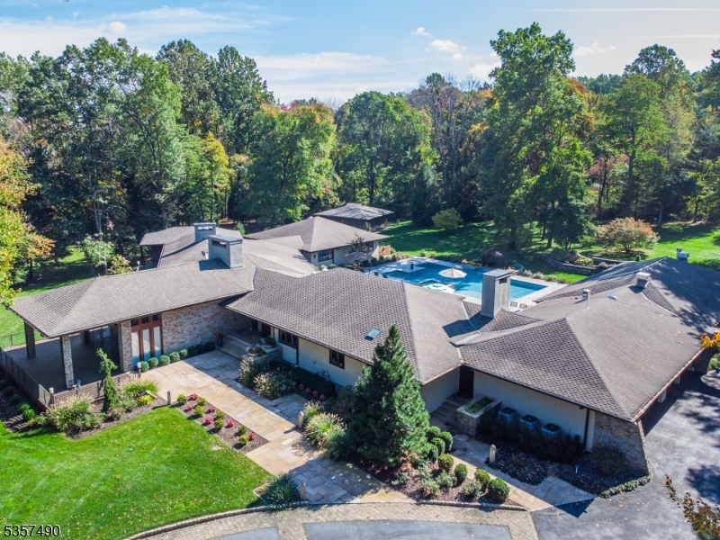 A true architectural gem, this sophisticated Mid-Century Modern style estate delivers refined luxury, unparalleled privacy and resort-style living all just minutes from shopping, dining and transit. Set behind a gated entrance on a quiet cul-de-sac, a convenient circular driveway offers ample guest parking. Designed for both grand entertaining and intimate living, the home showcases seamless indoor-outdoor flow with a collection of extraordinary amenities including a heated Anthony & Sylvan pool and spa with waterfall (2017), outdoor grilling island & bar, flat lush lawns, established perennial gardens, and a 50-foot screened pavilion with stunning gas fireplace perfect for alfresco gatherings. Inside, the home unfolds with architectural drama and thoughtful design across two expansive levels. Highlights include a dramatic foyer, a sun-filled chef's kitchen featuring custom Neff cabinetry, dual glass-enclosed offices, a spacious primary suite with a barrel-vaulted wood ceiling, and a stylish lower-level lounge with wine room. Also on the lower level is a private guest suite, exercise room, sauna, game room and workshops. Car enthusiasts will appreciate the heated four-car garage with modern glass doors. This is a rare offering that combines beauty, luxury and tranquility.