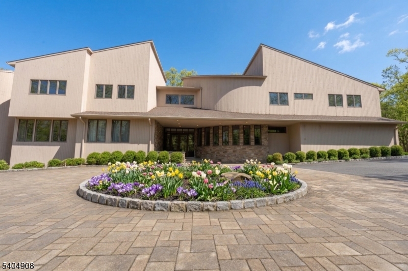 A rare architectural statement where scale, sophistication, and elevated luxury converge. Set on 3.7 private acres, the residence spans approximately 13,000 sq ft with 7 bdrms, 7 full baths and 2 half baths, designed for both grand entertaining and refined everyday living. From arrival, striking architectural lines, dramatic volume, and curated sight lines create a 'WOW' factor. The grand living room unfolds as a stunning open-concept space with soaring 32-ft ceilings, a sculptural spiral staircase, and a 2-sided 16-ft gas fireplace. Floor-to-ceiling windows flood the home with natural light, while views extend to the sun-drenched, heated indoor pool. The chef's kitchen pairs performance with modern design, featuring Wolf and Sub-Zero appliances, multiple ovens, wine refrigeration, coffee system, and premium finishes throughout. The main level also offers a private theater, gym, office, and first-floor au pair ensuite. The second level is anchored by a luxurious primary suite sanctuary with 20-ft ceilings, dual balconies, loft, sitting room, dual walk-in closets, and a spa-inspired bath with separate water closets and bidet. 5 addt'l bdrms include 3 ensuites and private balcony access.The lower level showcases the indoor pool, a 1,200-sq ft ballroom, dry sauna, full bath, and flexible space ideal for a wine room, cigar lounge, or recreation area. Additional highlights include a 4 car heated garage and dedicated elevator shaft. A truly one-of-a-kind Mendham estate!