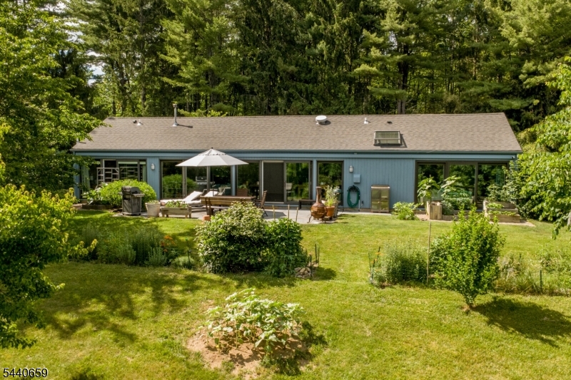 Sitting on over three private acres, this delightful single-level home embodies mid-century sensibilities and offers a peaceful retreat. Lush landscaping ushers you in to open-plan living with walls-of-windows and sliding glass doors framing beautiful views of the idyllic grounds. The chic and modern kitchen is awash in sunlight and offers stainless steel appliances, tile floor, abundant storage, and opens to the airy dining area. Enjoy the changing of the seasons from the bright living room with pellet stove, ready for the cool fall evenings to come! Designed for entertaining, sliding doors open to a stunning slate patio surrounded by blooming perennial beds. The primary bedroom suite is spacious and peaceful, with doors sliding open to the yard. Three large closets have built-in organizers, and the ensuite bathroom features a stone vanity and a walk-in shower with vaulted ceiling and skylight. Two additional bedrooms also feature floor-to-ceiling windows with outside access and share a smartly updated bathroom with radiant heated floor. A hall with storage, utilities, and laundry leads to the attached two-car garage with generator hook-up. Off the patio, a wrought iron gate opens to a verdant lawn with native plantings and pollinating flowers, and a finished outbuilding with HVAC and electric - ideal for an office, gym, or studio. Enjoy privacy, nature, and easy living in a beautifully maintained home with easy access to shopping, dining, and major commuter corridors.