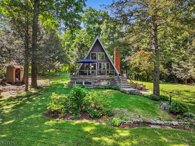 Tucked among the trees, where privacy is endless and nature takes center stage, lies an enchanting A-Frame unlike anything you've seen before. From the moment you step through the door, you're captivated by timeless charm, where every room tells a story. The main living area is warmed by a pellet stove, creating the perfect gathering place, while the character-filled kitchen showcases artistic touches rarely found in today's homes. A spacious dining room framed by picture windows captures peaceful woodland views, seamlessly bringing the beauty of nature indoors. Above, a loft-style bedroom offers a cozy retreat. The lower level, accessible from the side of the home a living room with a woodburning stove a wet bar, full bath, laundry area, and abundant storage. Step outside to your own private woodland sanctuary. A beautifully designed paver patio, charming pergola, and twinkling lights create a magical setting for entertaining or unwinding beneath the stars. Backing directly to state land, the property offers exceptional privacy and a breathtaking natural backdrop in every season. A rare bonus awaits across the street with an additional lot featuring a massive two-car garage complete with electric and water. Ample paved parking provides room for an RV, boat, recreational vehicles, or future projects. More than just a home, it's a retreat where every day feels worlds away from the ordinary.