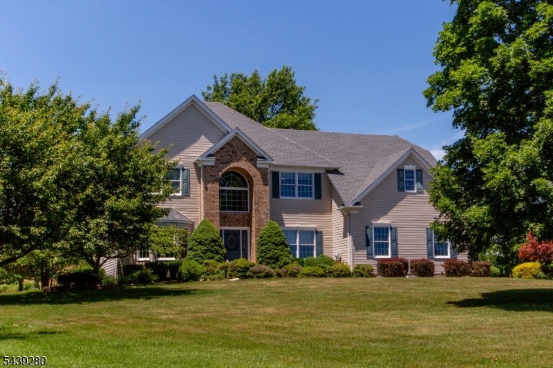 Set on 1.69 lush acres backing preserved farmland, this impeccably kept custom colonial blends serenity, privacy, and convenience just minutes from Flemington. A walkway edged by mature landscaping and flowering trees leads to a soaring two-story foyer. Sunlit oak hard-woods span the main level, guiding you to a generous eat-in kitchen with abundant cabinetry, pantry, and center island overlooking a bright breakfast room wrapped in windows with glass-paned doors leading to a shady stone patio perfect for morning coffee, birdsong, and glowing sunset views. The great room invites relaxed gathering with a wood-burning fireplace flanked by arched windows and a vaulted, skylit ceiling. A bay-windowed living room flows into the dining room for effortless entertaining. A French door reveals a quiet home office, while a main-level full bath adds flexibility. The mudroom with laundry and utility sink connects to the attached two-car garage. Upstairs, double doors unveil an expansive primary suite with walk-in closet and spa-like bath featuring soaking tub, glass shower, and dual vanity. Three additional bedrooms, each with oversized closets, share a crisp hall bath. A high-ceilinged full basement offers abundant dry storage and excellent finish potential. Outside, the graceful lawn and gardening shed invite play, planting, and quiet enjoyment. Near major commuting routes and downtown Flemington, this home delivers peace, privacy, and polished comfort close to every amenity.