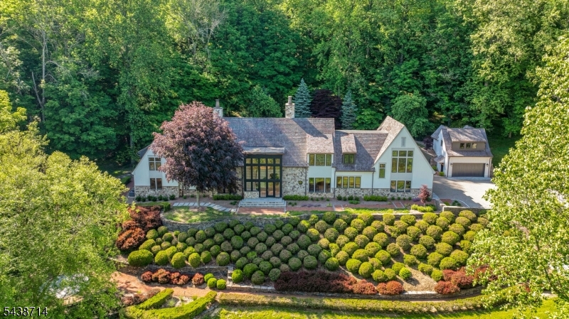 Set on 12.45 private acres within the prestigious Bernardsville Mountain enclave, surrounded by mature woodland and beautifully maintained grounds. Timeless European-inspired architecture, handcrafted stonework, soaring walls of glass, custom millwork, designer finishes, and European White Oak flooring define the residence throughout. Designed for everyday living and grand-scale entertaining, the home features 5 bedrooms, 6 full bathrooms, and 3 half bathrooms. The gourmet kitchen showcases a dramatic bookmatched Calacatta Oro stone feature wall, custom cabinetry, expansive center island, and adjoining butler's pantry. Multiple gathering spaces include a grand living room, formal dining room, private office, library-inspired retreat, and spacious family room. The luxurious primary suite offers a private lounge with wet bar, boutique-inspired dressing rooms, and a spa-like bath with a sculptural soaking tub, dual shower suites, and exquisite marble finishes. The lower level features a custom-crafted wine cellar, recreation spaces, and additional entertaining areas. A detached carriage house provides a private guest suite with full bath, wet bar and soaring ceiling. The attached garage accommodates up to 7 vehicles with lift capability. A rare offering combining exceptional craftsmanship, privacy, and luxury living, just moments from Bernardsville's renowned country clubs, equestrian amenities, fine dining, highly rated schools, and convenient access to New York City.