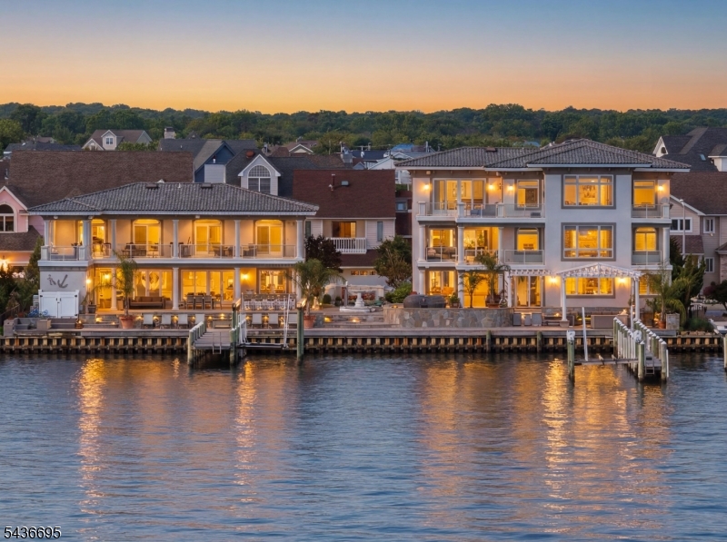 Waterfront compound. One purchase, two residences. The Toms River property includes a main house and detached guest residence on a protected waterfront lot with dual private docks and infinity pool. The main residence spans three floors connected by elevator, with working kitchen anchoring the first floor, dining and living areas scaled for entertaining, and a primary suite with sitting room, ensuite and expansive closet. Secondary bedrooms with multiple bath configurations occupy the second floor. The guest residence stands as a standalone four-bedroom home with dedicated kitchen, dining, living and covered patio. Outside, two boat docks service the water, an infinity pool commands the waterfront edge, outdoor bar and patio zones define entertaining spaces. Professional finishes throughout, heated gunite pool, two-car garage. Designed for year-round waterfront living and entertaining at scale. Twenty-three rooms total across both structures. Minutes to Toms River and NYC transit.
