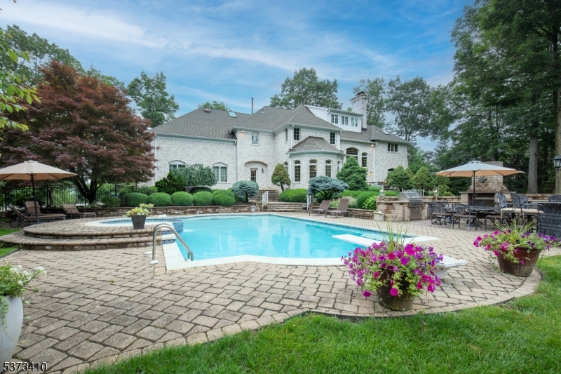 Set behind a gated paver driveway in one of Bernardsville's most desirable neighborhoods, this stately custom residence redefines luxury living with unparalleled craftsmanship, sophisticated interiors, and exceptional privacy. A gracious entry reveals soaring ceilings, elegant archways, and an effortless flow between formal and casual living spaces. The stunning conservatory features a deep coffered ceiling, marble fireplace, and French doors leading to a serene private patio. The paneled library with its own fireplace offers the perfect retreat for quiet reflection or work-from-home days.Upstairs, the luxurious primary suite is a true sanctuary, complete with a sitting room, fireplace, two walk-in closets, and a spa-like bath. Four additional bedrooms include two en-suites and a shared full bath. The versatile third level suite offers luxurious space for guests. The finished lower level is designed for entertainment and wellness, featuring a custom bar, two fitness rooms, and a game/media lounge. Outside, enjoy resort-style living with multiple patios, a built-in outdoor kitchen, and a sparkling gunite pool all set against a lush backdrop.Practical amenities include a three-car garage, updated HVAC systems, and a built-in generator. Located just minutes from downtown Bernardsville with top rated schools and trains to NYC, enjoy this rare opportunity to own a truly special estate home that blends timeless elegance with everyday comfort.