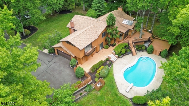 Nestled on over an acre of beautifully landscaped grounds in one of Scotch Plains' most sought-after neighborhoods, this custom contemporary home offers a rare combination of privacy, space, and architectural character. Soaring cathedral ceilings, walls of glass, skylights, and expansive living spaces fill the home with natural light and showcase picturesque wooded views from nearly every room. The flexible floor plan features 4 bedrooms, 3 full baths, a spacious living room, formal dining room, family room with fireplace, private library/home office with fireplace, and a walk-out lower level with recreation space, guest bedroom, full bath, and laundry room. The oversized primary suite offers a private balcony, walk-in closet, and spa-like bath with jetted tub, stall shower, and bidet. Outdoor living is equally impressive with a heated in-ground pool, multiple decks, screened porch, patios, mature landscaping, and exceptional privacy creating a true backyard retreat. Additional highlights include a 2-car attached garage, public water and sewer, natural gas service, central air, underground sprinklers, and a prime location close to top-rated Scotch Plains-Fanwood schools, parks, shopping, dining, and NYC transportation. An exceptional opportunity to personalize a distinctive home in a premier setting!