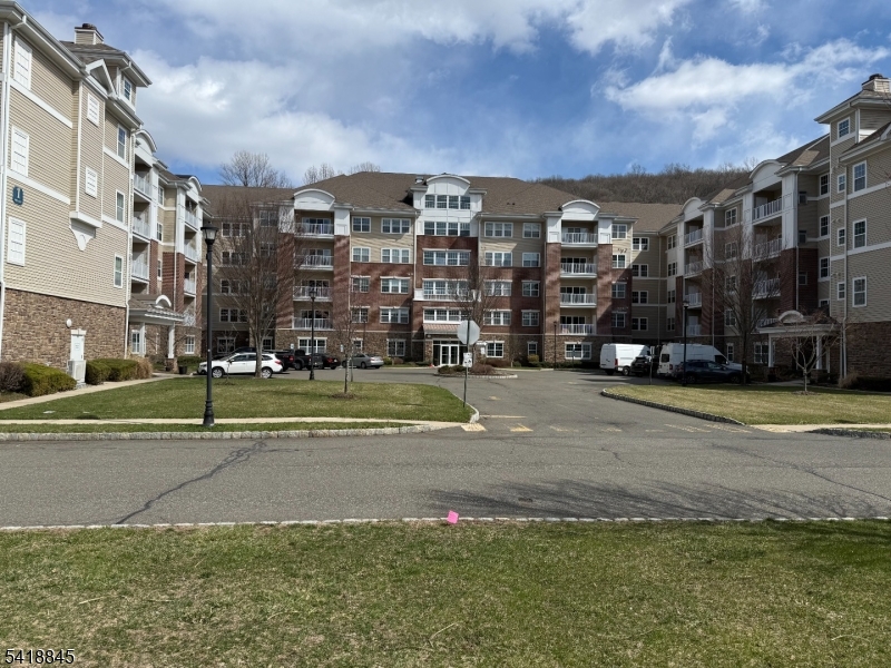 Largest 2 bedroom 2 bath model, 2119 SF Westbrook end-unit in Wanaque Reserve, a Del Webb 55+ active adult community, is in the newest building in the complex. This move-in ready home boasts hardwood flooring and a spacious 20x20 primary bedroom ensuite featuring a full bath, tray ceiling, and two walk-in closets. There's also a second bedroom, full bathroom, eat-in-kitchen with stainless steel appliances, granite countertops and a tiled backsplash. The living room, dining room, and den are highlighted by French doors for added elegance, and the living room's sliding doors lead out to a private balcony with seasonal views. Additional features include a larger den, larger laundry room and larger 2nd bedroom, upgrades such as three pot drawers. extra upper cabinets, a laundry area with countertop and cabinetry, wine refrigerator, new hot water heater, and new refrigerator. The home comes with two deeded parking spaces # 61 & 75, a 6x10 storage unit on the same floor #1F and 24-hour security. Residents enjoy access to a 20,000 SF clubhouse offering amenities like a cafe, ballroom, gym, theater, sauna, indoor and outdoor pools, plus more than 45 clubs & activities, including travel club (cruises, trips, casino outings), tennis, pickleball, canasta, poker, golf, and more. WR provides residents with a luxurious lifestyle focused on modern comforts, security and community spirit. Recent renovations have created a fresh, updated living environment.