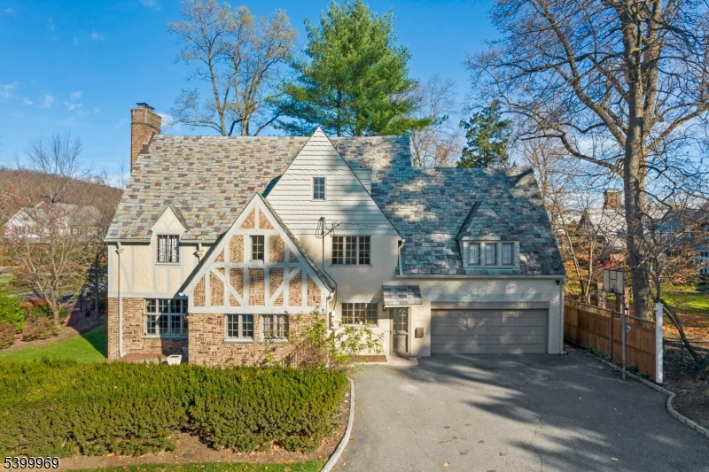 This light-filled Tudor blends timeless character with modern comfort in Montclair's prestigious Estate Section.  A dramatic sunken living room with fireplace flows into a formal dining room with floor-to-ceiling windows and access to enchanting patios and landscaped gardens. A spacious family room, eat-in kitchen with butler's pantry, and powder room complete the main level. The second floor provides flexible living with a generous primary suite and attached office or optional sixth bedroom, along with three additional bedrooms including a two-room suite with its own bath, plus a hall bath. The third floor provides versatile bonus space with a paneled room, full bath, and a billiards room, office, or gym. Finished lower level space includes a powder room, laundry, and ample storage. Outside, enjoy magical patios for entertaining and a tucked-away play area with play set. Just minutes to downtown shops, dining, and entertainment, plus a direct NYC train for effortless commuting. Don't miss out on this rare opportunity to enjoy all that Montclair has to offer!