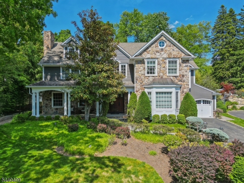 Welcome to 19 Hilltop Road, Short Hills -  a home that offers timeless elegance, exceptional craftsmanship, and modern amenities throughout. A grand two-story foyer with a curved staircase sets the tone for this beautifully appointed home. The formal living room features a wood-burning fireplace, custom moldings and built-ins, while the dining room is highlighted by a bay window and French doors opening to the patio for seamless indoor-outdoor entertaining. The chef's kitchen is equipped with a center island, prep sink, beverage refrigerator, Viking range, and patio access, and opens to a spacious family room with coffered ceiling, gas fireplace and built-ins. A first-floor bedroom with an en-suite bath provides flexible space for guests or a home office. Upstairs, the luxurious primary suite features a tray ceiling, gas fireplace, private balcony, large walk-in closets and spa-like bath with a jetted tub, stall shower, dual vanities, and water closet. Additional bedrooms, a 3rd floor bonus bedroom, and 2nd floor laundry offer comfortable, functional living. The finished lower level includes a recreation area, wet bar, beverage refrigerator, exercise space with projector and screen, and full bath. Multiple French doors lead to a spacious patio overlooking the private, beautifully landscaped fenced-in backyard, ideal for entertaining, play, and relaxation. Additional highlights include a welcoming front porch, attached two-car garage, mudroom, and abundant storage throughout.