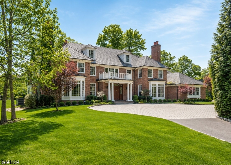 Tucked behind mature plantings on more than an acre of level private grounds, this distinguished all brick Georgian colonial is the work of acclaimed architect John James. Light pours through every room of this impeccably built residence, where a soaring two-story foyer sets the tone for the scale and craftsmanship found throughout. Generously sized rooms showcase rich architectural millwork, lofty ceilings, refined finishes and warm hardwood floors at every turn. At the heart of the home, a chef's eat-in kitchen pairs premium appliances with effortless everyday function, while a serene primary suite captures lovely views and a richly paneled custom library offers a quiet retreat. The inviting family room gathers around a striking rustic stone fireplace, and outdoors a generous bluestone terrace opens to manicured lawns beneath an enduring Vermont slate roof. A convenient three-stop elevator links the lower, first and second floors with ease, and ample room remains to create additional bedrooms and baths in the future. Served by the acclaimed Millburn Township school system, this property sits just moments from Midtown Direct rail service to Manhattan, an array of vibrant shops and fine restaurants, the Canoe Brook Country Club and the world-renowned Mall at Short Hills. Homes of this caliber, in a setting this rare and this beautifully private, seldom come to market in one of New Jersey's most coveted and highly sought after residential enclaves and communities.