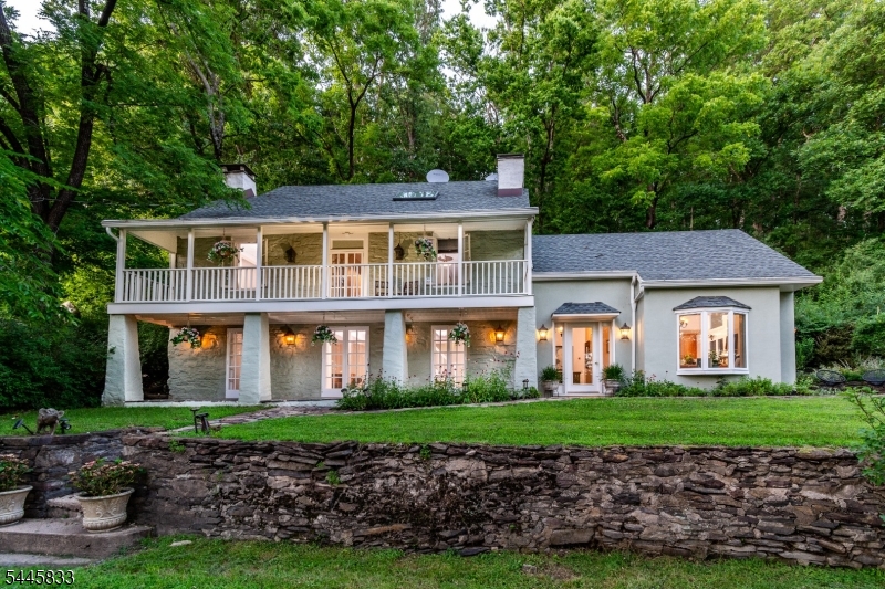 Dating to the late 1700s, this remarkable stone home sits amid beautiful, scenic acreage. Stacked stone walls, a graceful semicircular gravel driveway, and a winding fieldstone walkway create an unforgettable first impression. Covered front porches offer serene vistas of the expansive front yard. A stone pathway leads to the lower porch, framed by handsome tapered posts and opens through triple French doors to the living and dining rooms. An impressive foyer with terrazzo tile flooring leads to a remodeled open kitchen with a large window over the sink and cathedral beamed ceilings, while dramatic angled transom windows draw in natural light and frame views of the surrounding landscape. A cozy breakfast nook features an island for prep and seating. The living room is open to the dining area, all anchored by a striking fireplace with a substantial wood mantel, exposed beams, slate flooring. A practical first-floor layout blends modern convenience with the home's enduring character. Two bedrooms upstairs offer hardwood flooring and exposed beams. An impressive stone wall with an original fireplace and built-ins grace bedroom two. the entire top floor is reserved for a private primary suite complete with its own outdoor deck, office nook, vaulted ceiling, hardwood flooring, a double closet and an en-suite bath. Rich in history, the house lives beautifully for today, balancing period architecture with comfortable gathering spaces and timeless style.