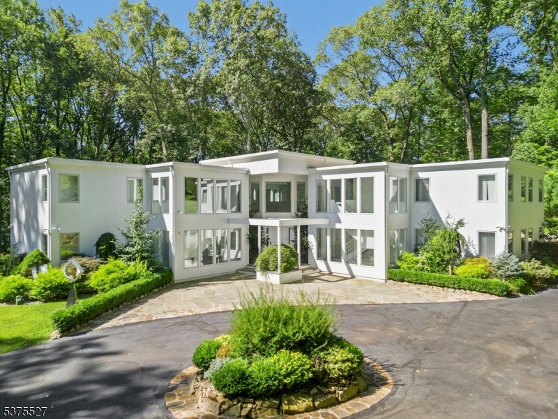 LIVE LIKE YOU JUST STEPPED OUT OF THE PAGES OF ARCHITECTURAL DIGEST IN THIS EXTRAORDINARY MODERN ESTATE NESTLED ON OVER 5 PRIVATE ACRES IN BERNARDSVILLE, NEW JERSEY. EXCEPTIONAL CRAFTSMANSHIP AND SOPHISTICATED DESIGN DEFINE EVERY CORNER OF THIS HOME. SOARING CEILINGS AND WALLS OF GLASS BATHE THE INTERIORS IN NATURAL LIGHT, WHILE A DRAMATIC TWO-STORY MARBLE FOYER WITH A GRAND CHANDELIER WELCOMES YOU WITH ELEGANCE AT FIRST GLANCE.THE DESIGNER KITCHEN FLOWS EFFORTLESSLY INTO A STRIKING DINING AND LIVING SPACE PERFECT FOR BOTH INTIMATE GATHERINGS AND GRAND ENTERTAINING. ENJOY THE WHOLE-HOME SURROUND SOUND SYSTEM INDOORS AND OUT.THE MAIN LEVEL IS DOMINATED BY A BREATHTAKING TWO-STORY PRIMARY SUITE, COMPLETE WITH A LOFT, DUAL WALK-IN CLOSETS, AND A SPA-INSPIRED BATH FEATURING A FREESTANDING TUB. UPSTAIRS, A LOFTED STUDY OPENS ON TO A PRIVATE DECK, AND A BRIDGE WALKWAY LEADS TO A FAMILY ROOM WITH A WET BAR, OAK FLOORS, AND TWO ADDITIONAL ARTFULLY APPOINTED CUSTOM DESIGNED BEDROOMSTHE WALK OUT LOWER LEVEL OFFERS VERSATILITY AND LUXURY: A FULL DESIGNER KITCHEN WITH COUNTER SEATING, MEDIA AND RECREATION AREAS, BILLIARDS CORNER, ART STUDIO, AND A GUEST SUITE WITH ENSUITE BATH. STEP OUT TO THE PATIO AND HOT TUB YOUR PRIVATE RETREAT BACKED BY NATURE'S PEACE.EQUIPPED WITH A VIVINT SMART ALARM AND AN ECO-FRIENDLY MOSQUITO CONTROL SYSTEM. THIS ESTATE IS MORE THAN A HOME, IT'S A LIFESTYLE AND A SANCTUARY.