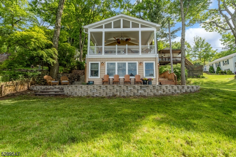Stylish lakefront. Spectacular lake view from the covered porch. Enjoy those lazy summer days and evenings for dining and lounging around the gas firepit. An open floorplan designed to entertain. Custom well-appointed kitchen boasting stainless appliances, wood cabinetry, granite countertops, and a breakfast bar that opens to the living/dining room with views to the gas fireplace and covered porch. This 5-bedroom home offers a 1st-floor full bedroom w/full bath in the hall and first-floor laundry rm. 4 additional bedrooms include the primary bedroom with a walk-in closet and ensuite bath facing the lake. 3 additional bedrooms and a full guest bath. The finished lower level offers a flexible floor plan to add a kitchen as there is a full bath and a spacious open floor plan for your lakeside living. Two sets of glass slider doors lead out to the patio overlooking the lake. So many interior and exterior details that make this home maintenance-free! Be in for this summer and enjoy NJ's largest lake, just one hour to NYC with local rail service. Walk to town location for restaurants, shops, house of worship, and nearby town park. Enjoy motor boats, kayaks, jet skis, and more as this community offers scenic year-round living with access to hiking, biking, golf/tennis resorts and winter activities on the lake. This home shares an open common area, lakefront, and dock with the opportunity to purchase the ranch home "live in one, rent out the other"! Main lake location!