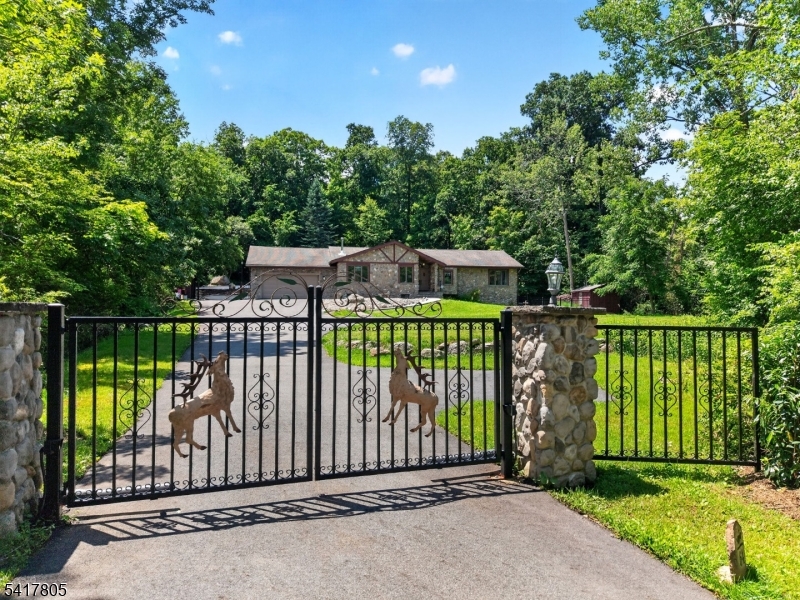 Welcome to this beautifully maintained custom raised ranch. Nestled on 1.5 acres surrounded by mature trees for exceptional privacy, this home offers a rustic mountain setting with a resort feel in Ringwood's Stonetown section, just one hour from NYC. An automated entry gate leads to a 2-car garage, multi-car driveway, and a striking fieldstone exterior accented by a custom front door with stained glass. Inside, the open layout showcases vaulted and cathedral ceilings, updated lighting, motion sensors, and durable luxury vinyl flooring throughout. Enjoy expansive living spaces, a home office, a family room with a fireplace, and a modern kitchen with updated appliances. The primary en-suite features a walk-in closet, while a separate addition with two bedrooms and a full bath provides a flexible layout to accommodate a variety of living arrangements. The lower level offers a renovated laundry room and abundant storage. Modern infrastructure includes a 5-year-old boiler, updated central AC with Nest/Honeywell thermostats, a split unit in the family room, an above-ground oil tank, and a water softener. The backyard is an outdoor retreat featuring abundant patio space, a massive 40' x 30' heated in-ground pool, a private "Sun Pad" overlooking the entire property, and both a gardening shed and a wood storage shed. Conveniently located just minutes from Ringwood State Park, Monksville Reservoir, and Lake Riconda for hiking, boating, and fishing. Move-in ready with quality upgrades!